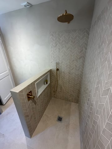 Rénovation salle de bain haut de gamme à Fréjus : douche à l'italienne en carrelage chevron grand format avec robinetterie laiton brossé et niche sur-mesure